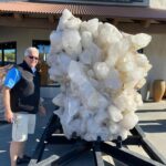 man standing next to giant crystal at rock and mineral show